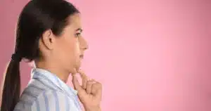 Woman in profile touching her chin, showing a double chin—ideal for Kybella treatment—against a pink background in Las Vegas, NV.